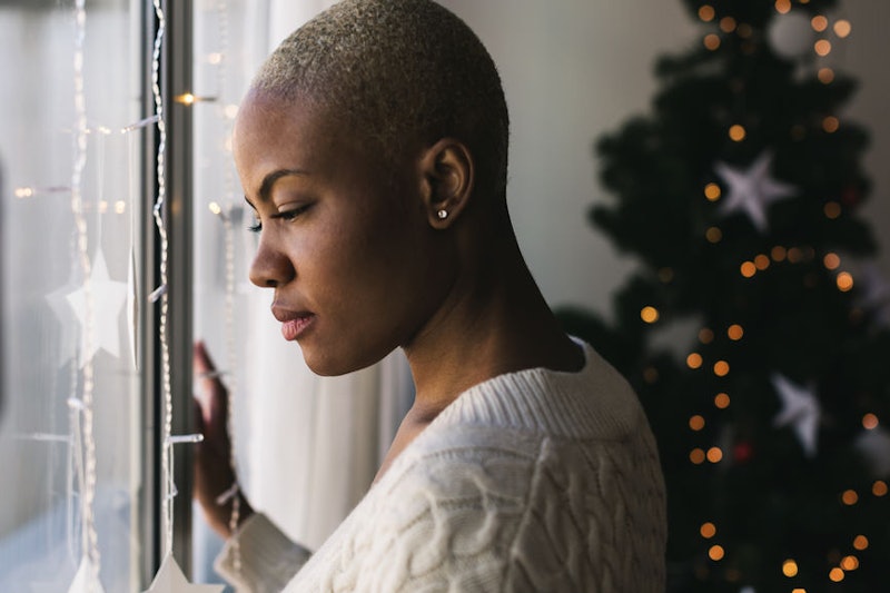 A woman with a shaved head looks out the window at christmas time, coping with grief during the holi...