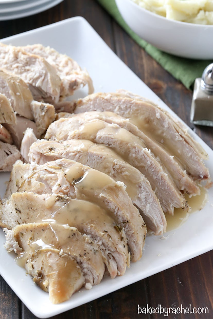 sliced turkey with gravy layered on top presented in a white square dish on a wooden table