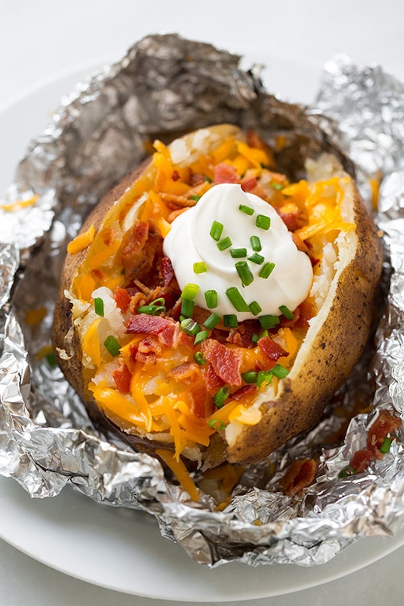 baked potato with shredded cheddar cheese, bacon, chives and sour cream presented in tinfoil on a pl...