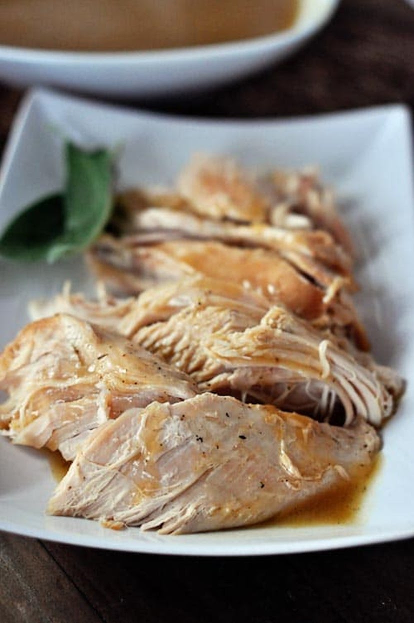 close up of cut up turkey with gravy drizzled over on a plate with a green leaf garnish on the side