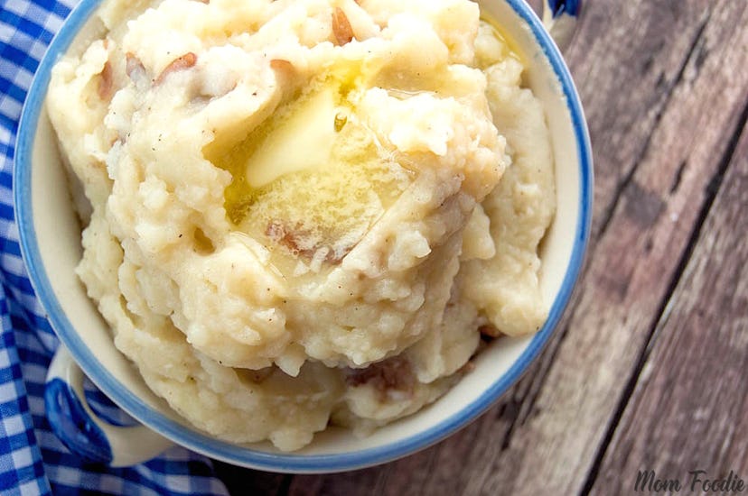 Bowl of clumpy mashed potatoes on a wooden table with blue and white plaid dishcloth to the left of ...