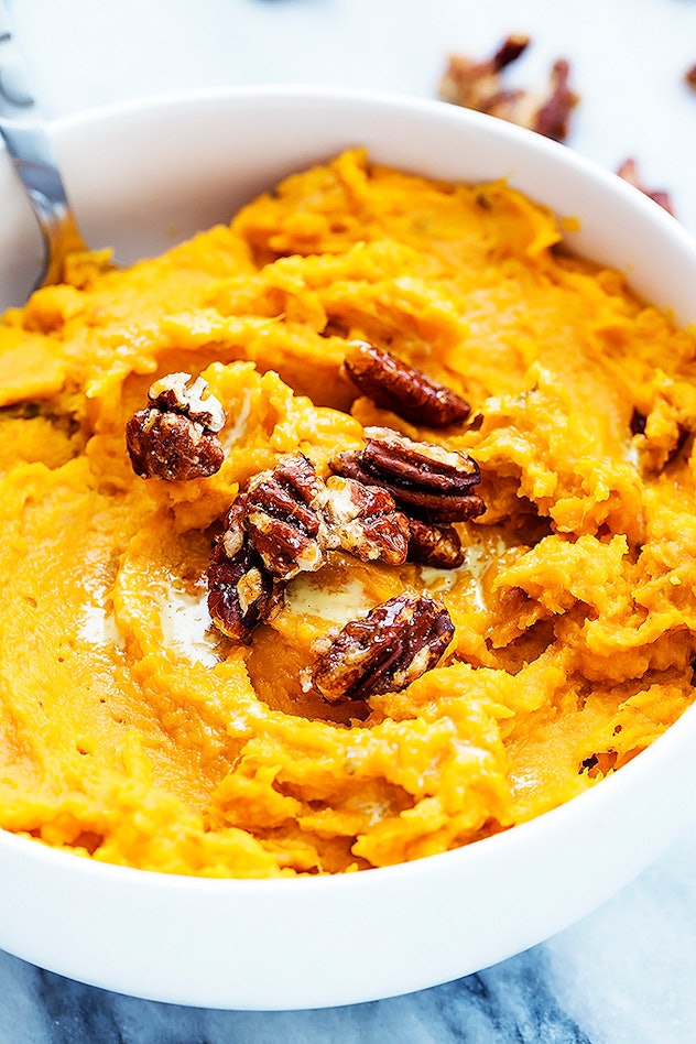 close up of white bowl with creamy orange sweet potatoes with walnuts 
