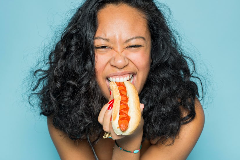Young girl eating a high-cholesterol hot dog with ketchup