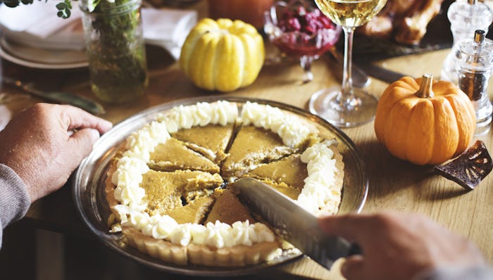 A man cutting a pumpkin pie on a dinner table decorated for Thanksgiving.