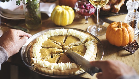 A man cutting a pumpkin pie on a dinner table decorated for Thanksgiving.