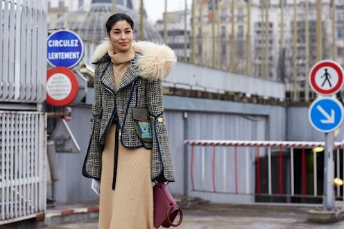 A model wearing a winter coat, a beige dress and a maroon bag while standing outside in the winter