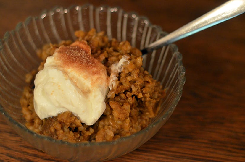 Glass bowl of oats topped with a dollop of white cream on wooden table with spoon sticking out