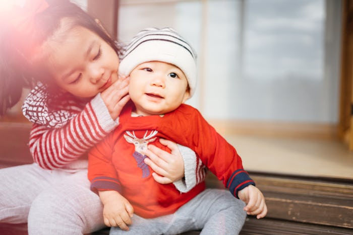 A toddler caressing and holding a small baby who was born in the winter