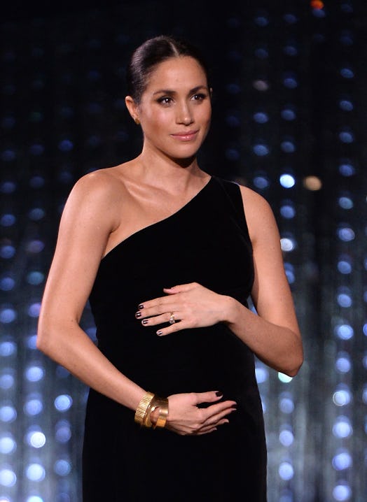 Meghan Markle wearing a black one-shoulder Givenchy dress at the British Fashion Awards holding her ...