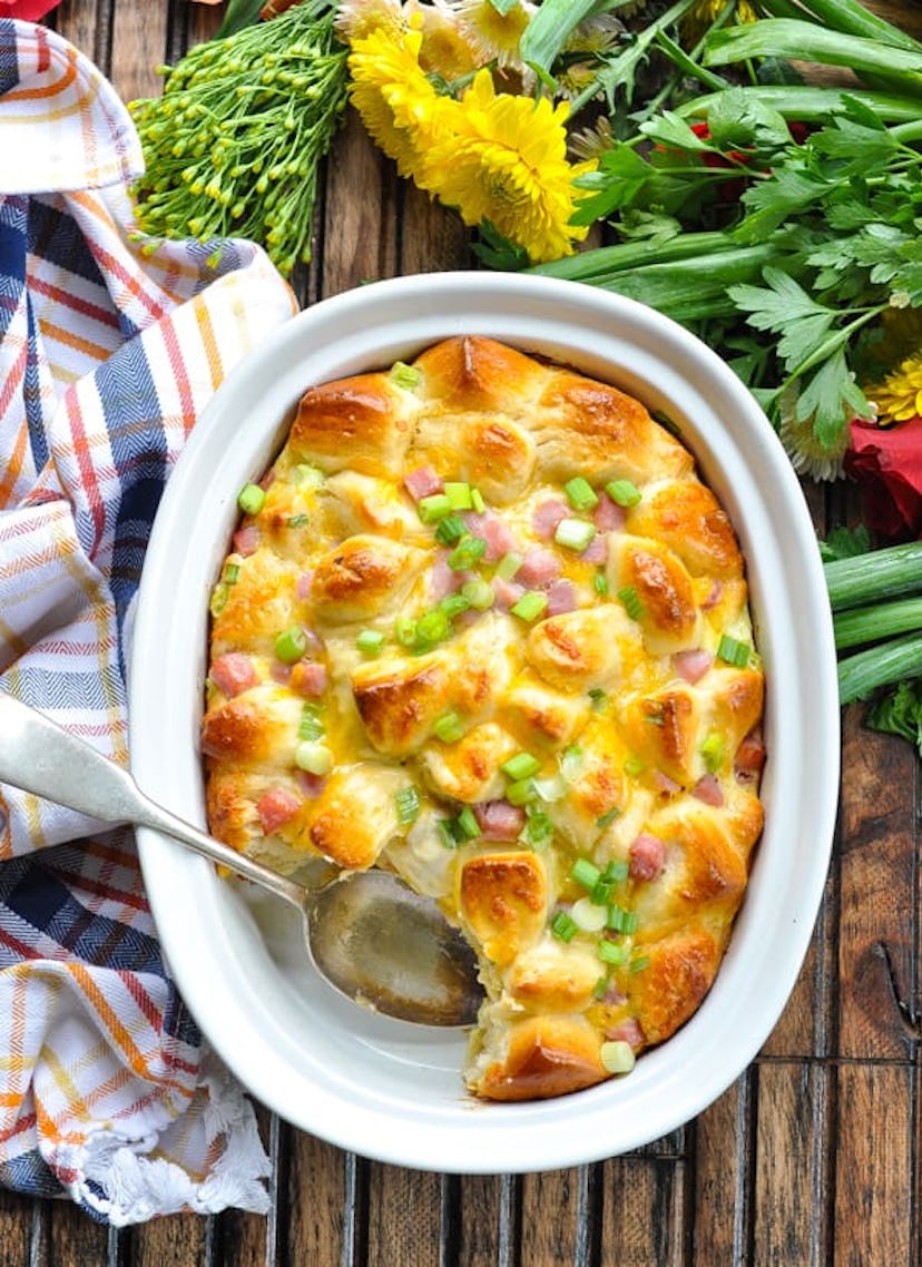 white dish pan full of ham, egg, and cheese monkey bread set on a wooden table with flowers in backg...