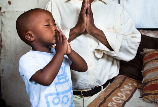 A toddler holding his hands in prayer next to his father who is also praying