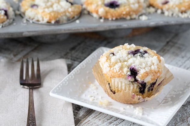 blueberry muffin on square plate with muffin tray in backgroun