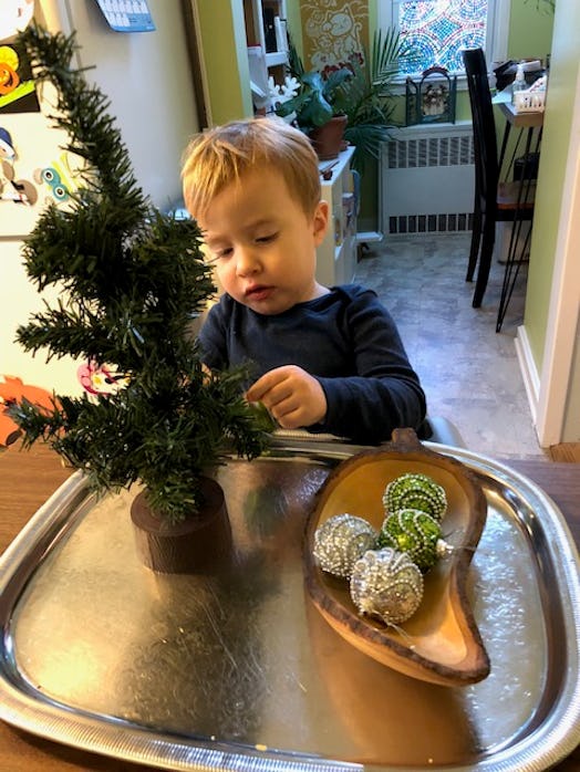A boy toddler decorating a small Christmas tree with green and white ornaments