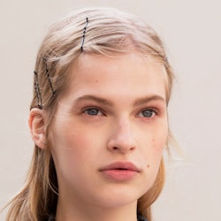 A close-up of a blonde model's face with a hairstyle with pins you'll definitely see in 2019, accord...