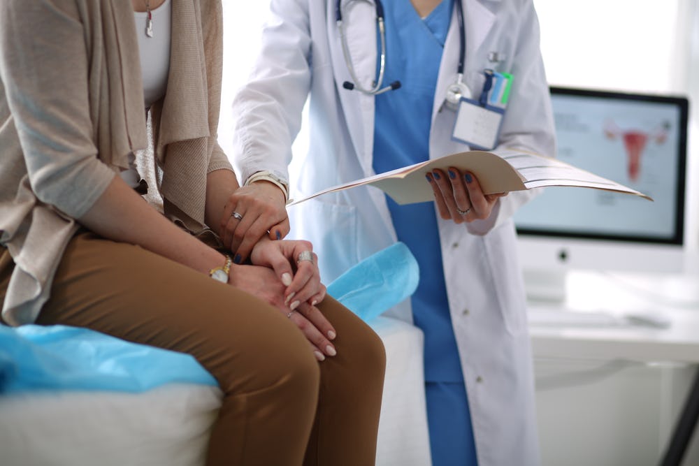 A woman sitting on the examination table in a doctors office getting a breast cancer check up
