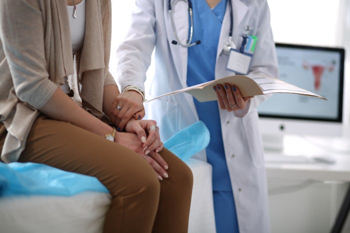 A woman sitting on the examination table in a doctors office getting a breast cancer check up