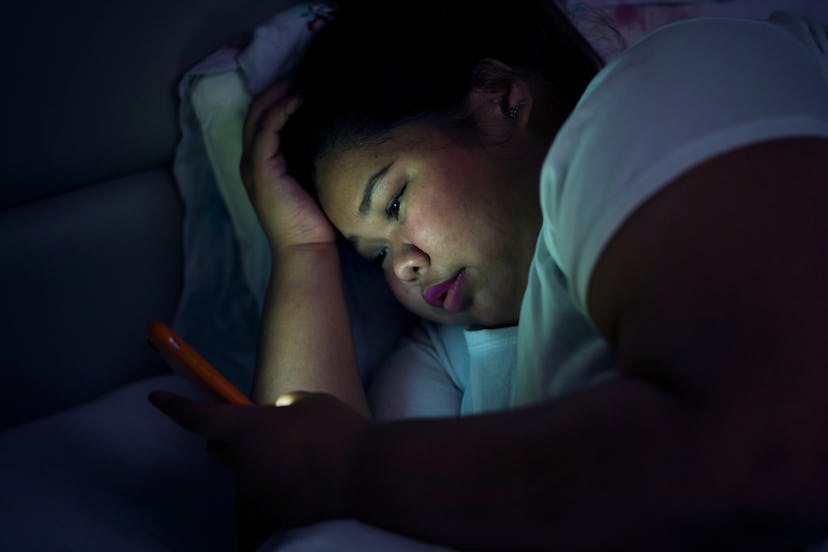 Sad girl on her phone in the dark of her bedroom experiencing anxiety