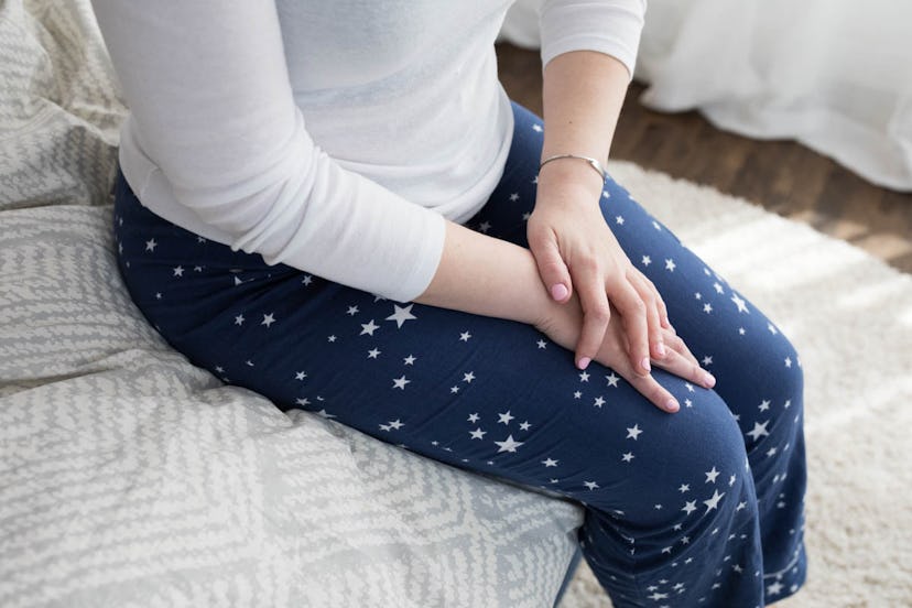 A woman sits on her bed in star-patterned pajamas, showing visible discomfort, with hands crossed ov...