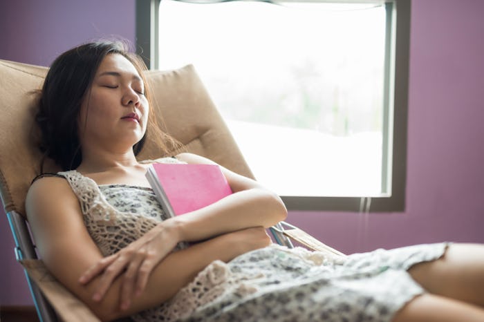 woman with arms crossed holding a book while sleeping in reclined chair
