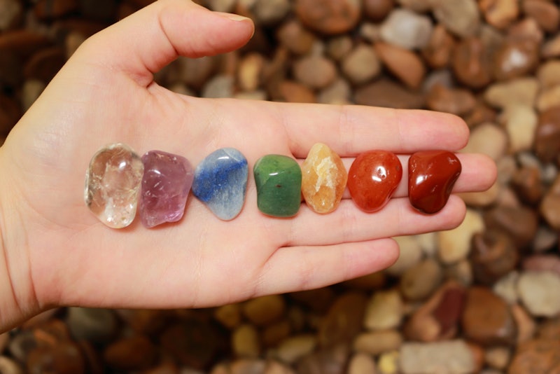 Seven different colored pieces of crystal placed on a person's hand palm