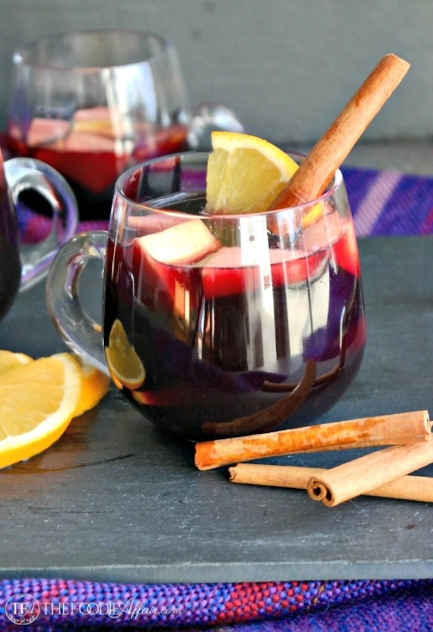 Glass mug of sangria with a cinnamon stick, sliced oranges, and apples inside