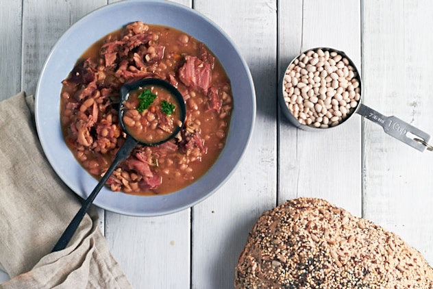 Bowl of navy bean soup next to a measuring cup full of uncooked beans