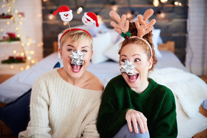 Two girls laugh in their bedroom dressed festive for Christmas, while one wears reindeer antlers and...