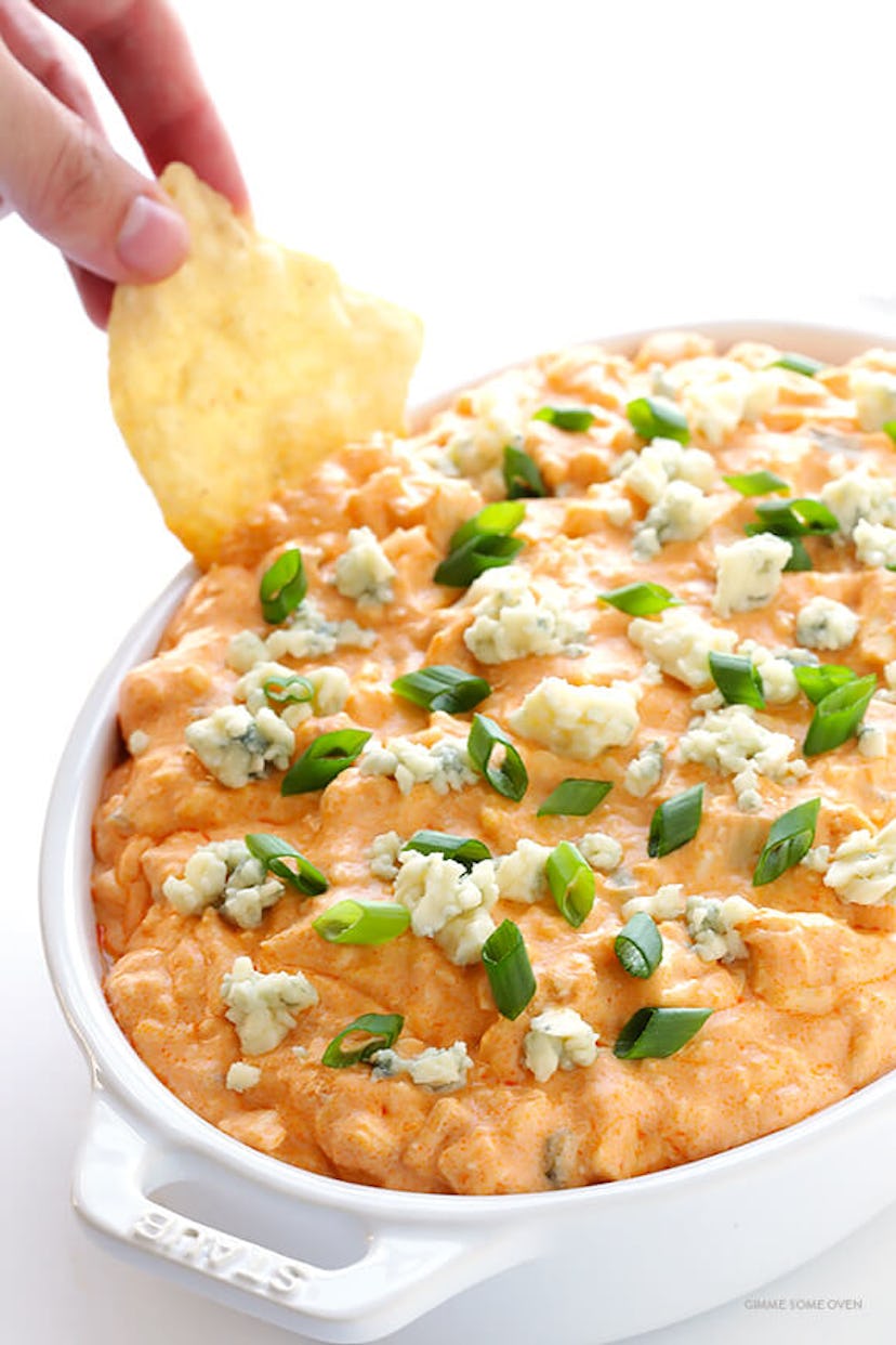 A tortilla chip scooping out buffalo chicken dip from a white pan