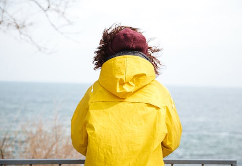 A womane experiencing loneliness and anxiety stands in a white rain coat and looks at the city sky l...