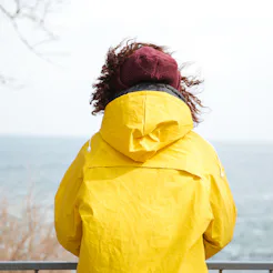 A womane experiencing loneliness and anxiety stands in a white rain coat and looks at the city sky l...