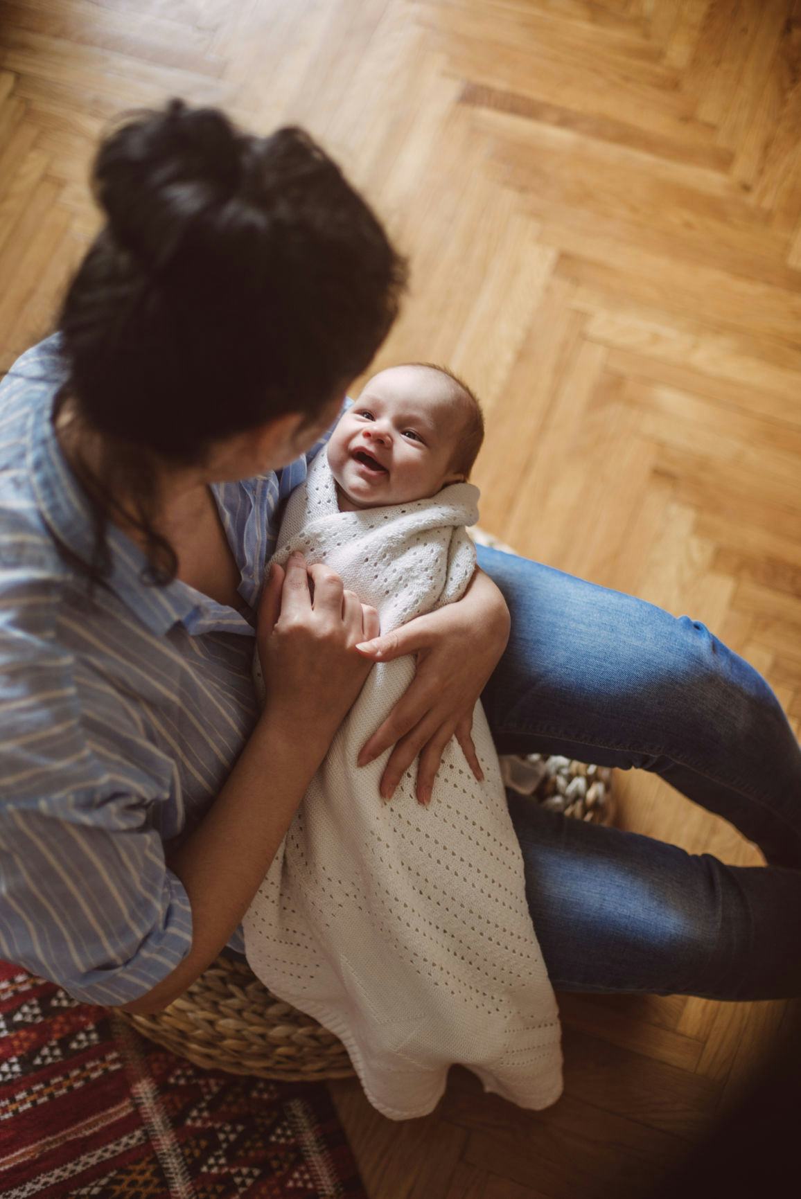 A mother sitting on a chair holding her swaddled newborn baby