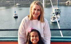 A woman with her six-year-old daughter in a marina with boats behind them 