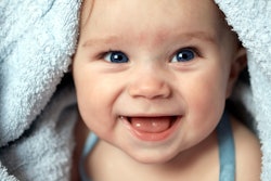 Close up of baby underneath blue blanket smiling at the camera, in an article about new year baby na...