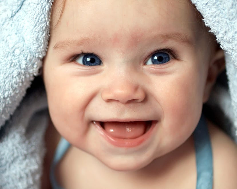 Close up of baby underneath blue blanket smiling at the camera, in an article about new year baby na...