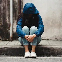 A young female struggling with loneliness wearing a blue hoodie covering her face while sitting on a...