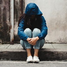 A young female struggling with loneliness wearing a blue hoodie covering her face while sitting on a...