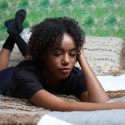 A lonely woman lying in bed on her stomach in a black shirt and black socks