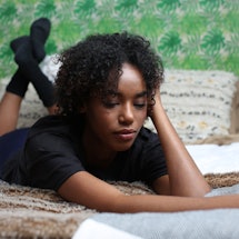 A lonely woman lying in bed on her stomach in a black shirt and black socks
