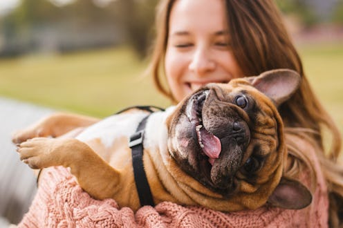 A woman holds her dog who is smiling with his tongue out.