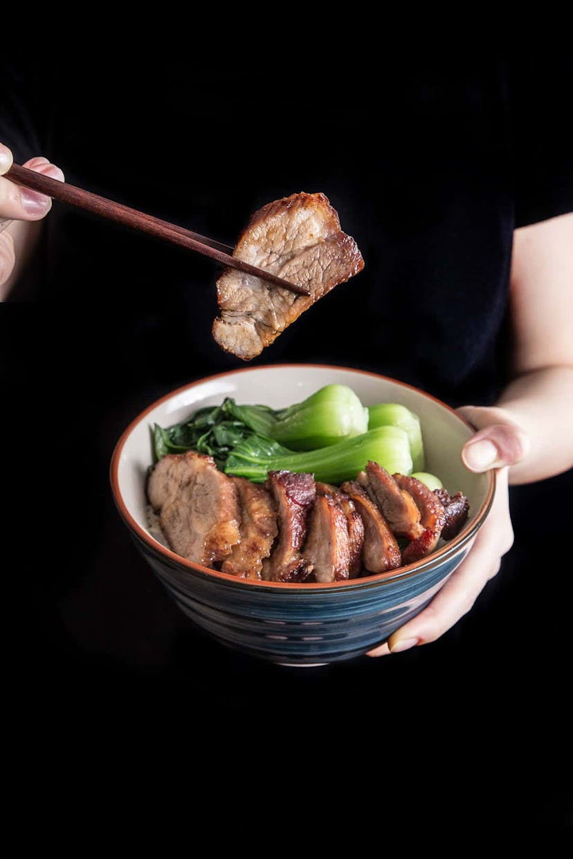 close up of someone holding up bowl and slice of pork with chopsticks