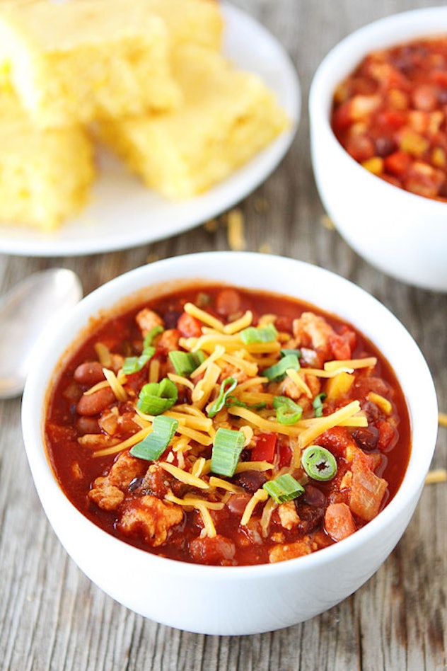 A white bowl full of red soup with shredded cheese on top 