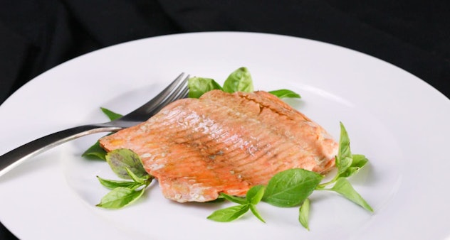 cooked salmon with green garnish on a white plate with a silver fork to the left of the salmon.