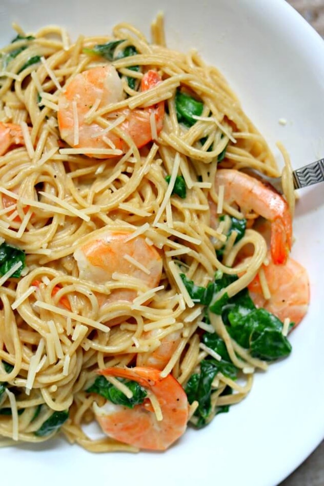 close up of shrimp on pasta with a white sauce and greens on plate