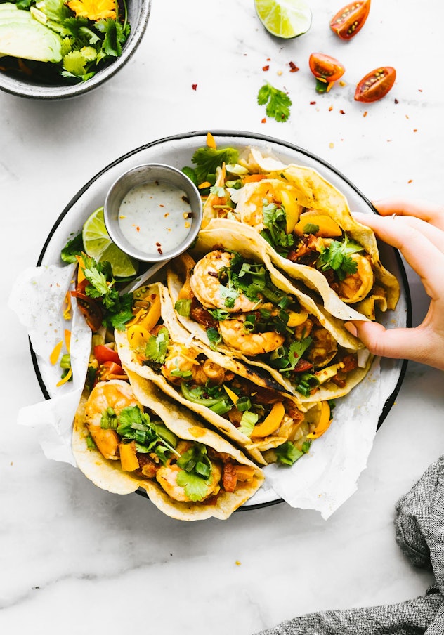Aerial shot of four tacos with shrimp, cilantro, tomatoes and avocado on a place