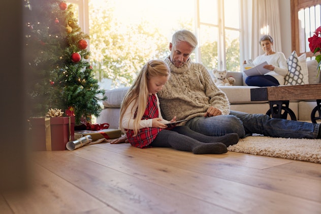 A grandfather playing on the floor with his granddaughter next to a Christmas tree 