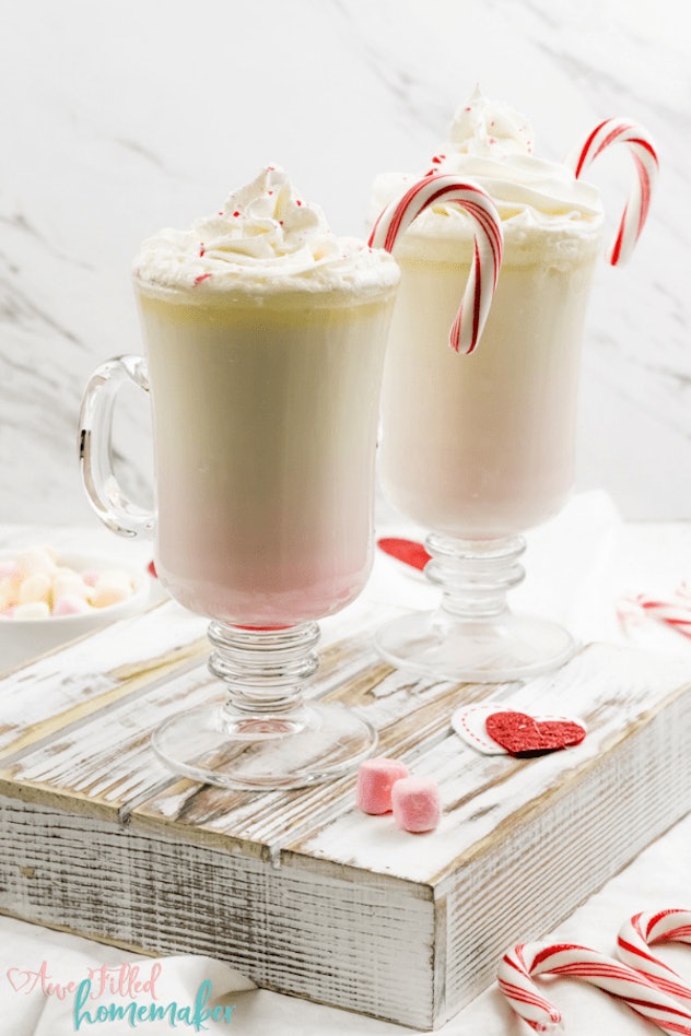 two clear mugs of white hot chocolate with whipped cream and candy canes in the glass
