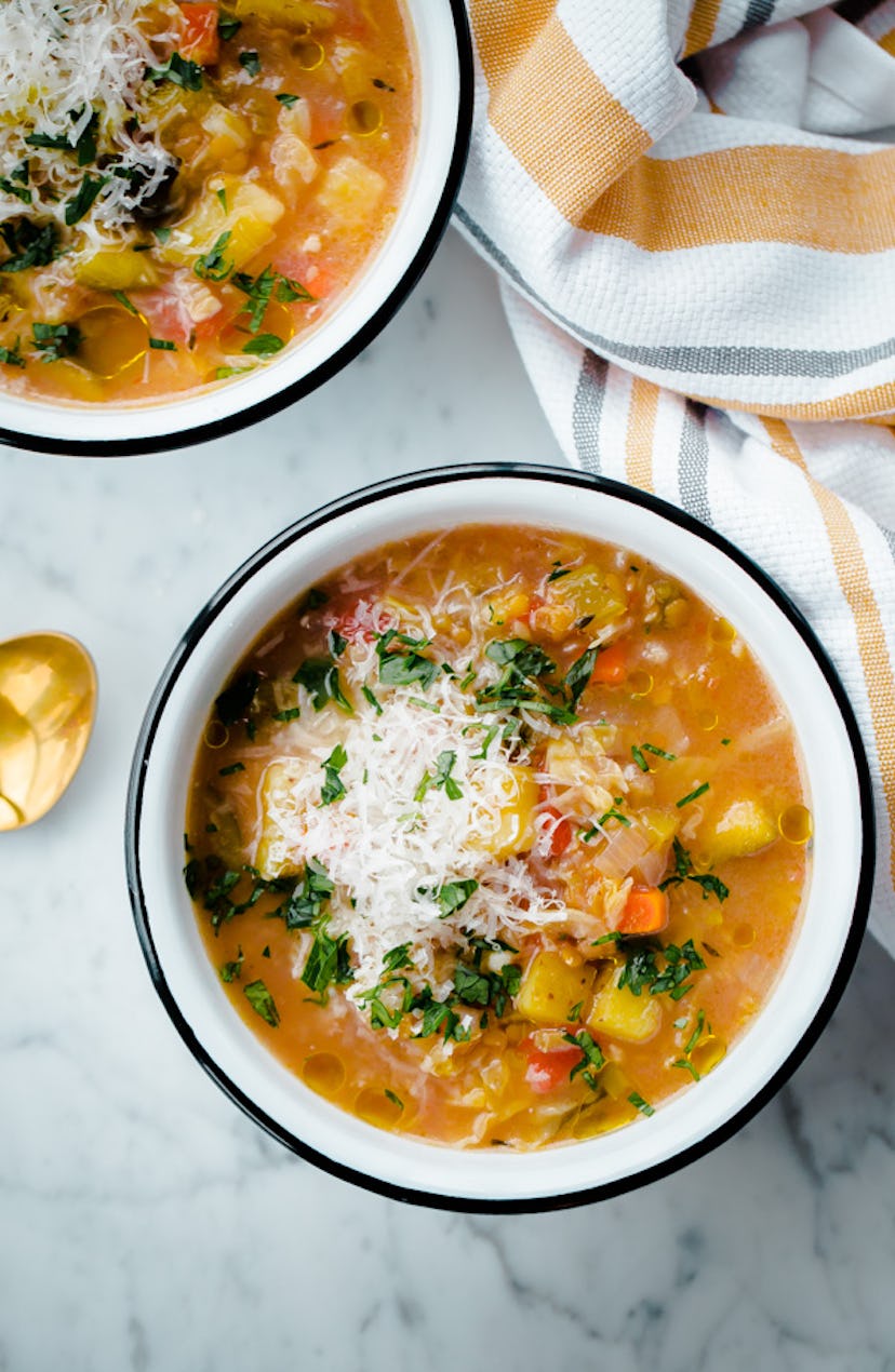 Two bowls full of a thin orange soup with vegetables