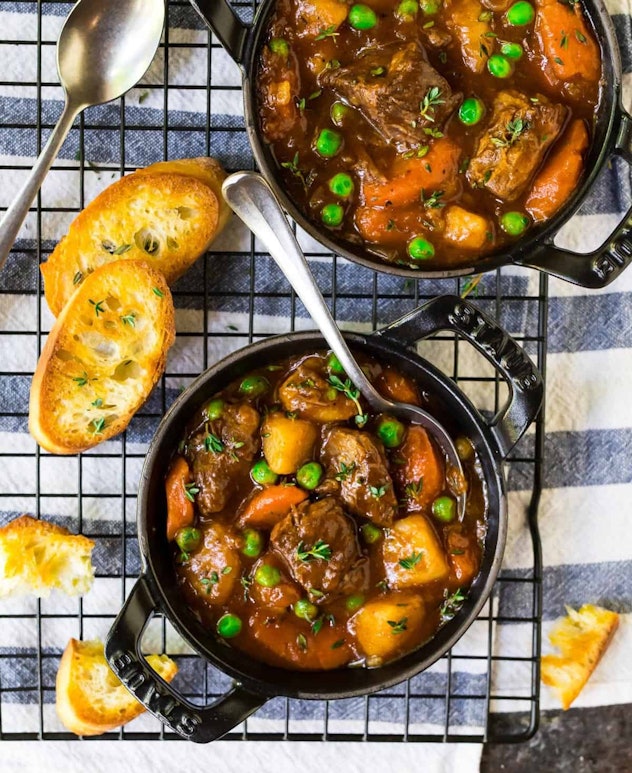 aerial view of two pots of beef stew with potatoes, peas, and carrots on cooling rack. slices of toa...