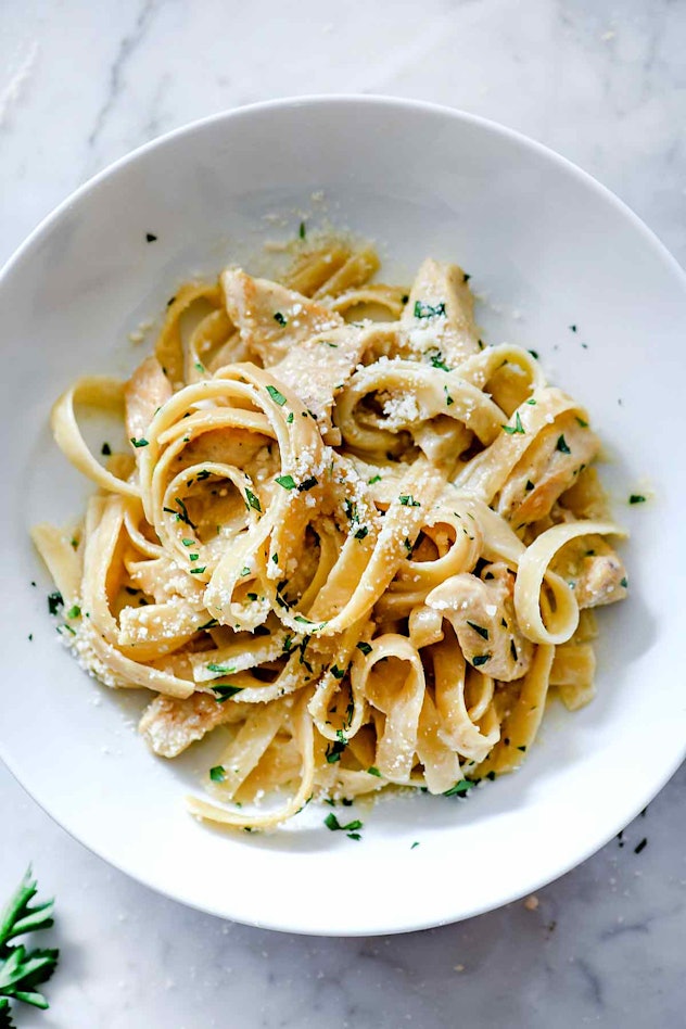 fettuccine pasta in a white sauce with chicken, sprinkled with cheese and garnished with parsley on ...