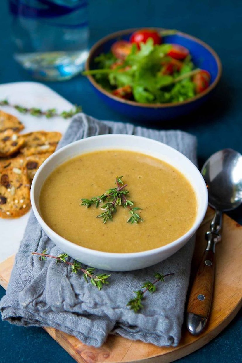 bowl of brown mushroom soup with rosemary garnish in a bowl on a cloth placed on top of a wooden cut...